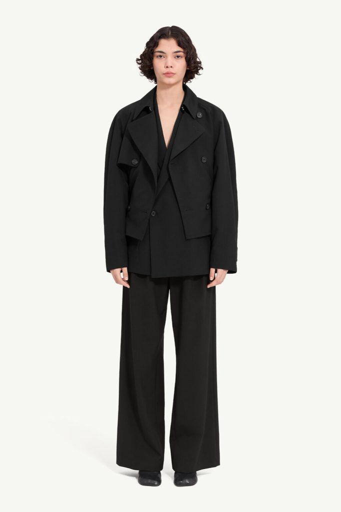 Person wearing an oversized black blazer over a matching black suit with wide-leg trousers, facing the camera against a light background.