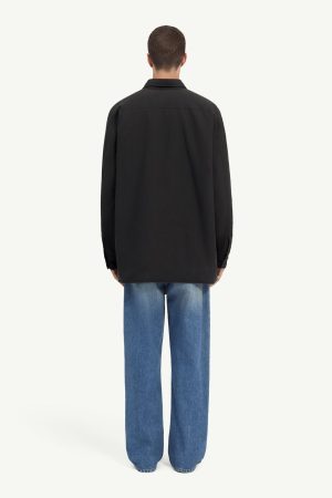 Back view of a person wearing a loose black jacket and blue jeans, standing against a light background.