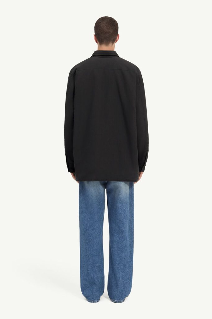 Back view of a person wearing a loose black jacket and blue jeans, standing against a light background.