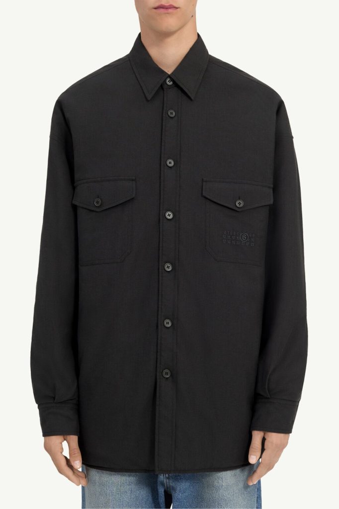 Black button-down shirt/jacket with two chest flap pockets worn by a person, dark and minimalist.