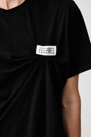 Close-up of a black T-shirt with a small white tag on the chest, showing a grid of numbers and a circled 6.