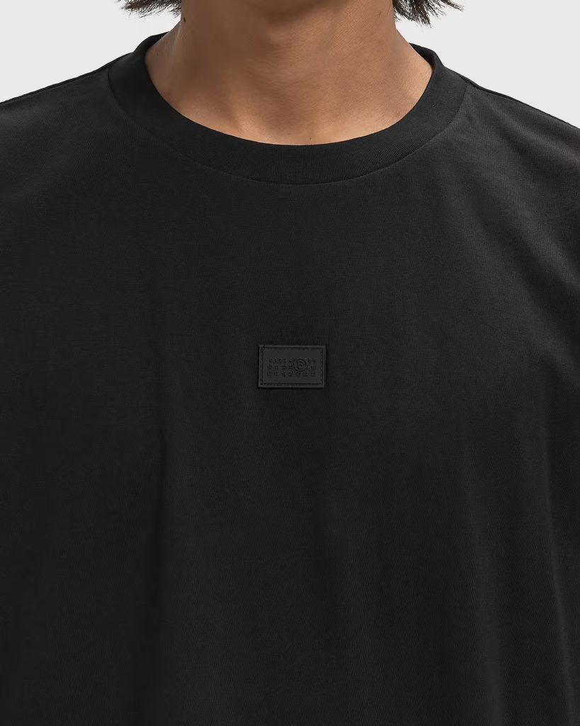 Close-up of a black crew-neck T-shirt with a small rectangular label on the chest area.