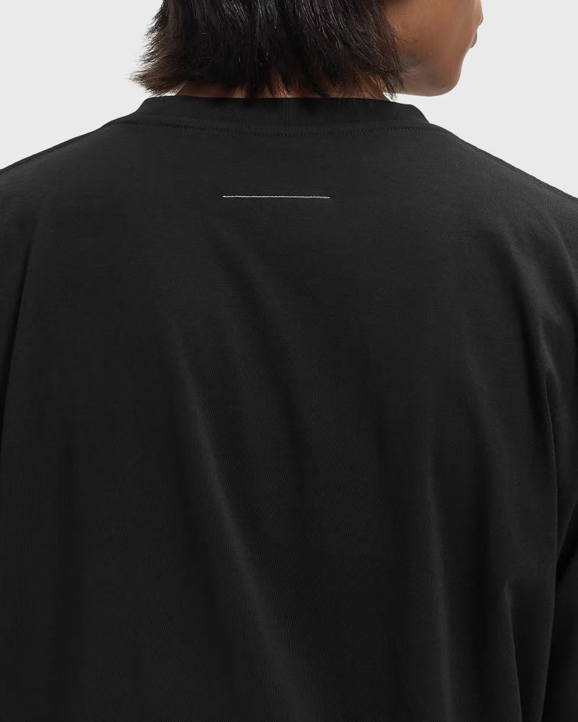 Back view of a person wearing a black collared shirt, featuring a small white horizontal stitch on the upper back.