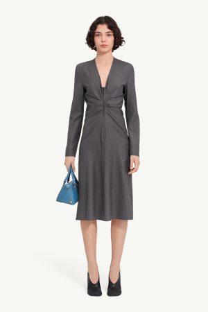Woman in a knee-length gray zip-front dress holding a blue handbag, wearing black heels, facing front.