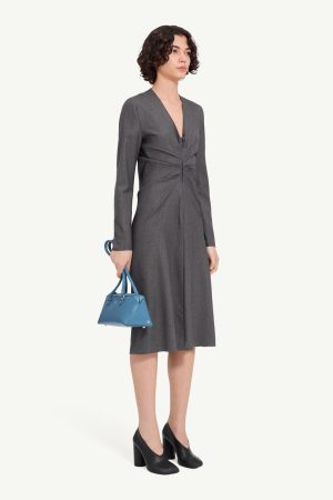 Woman in a knee-length grey V-neck dress, black chunky-heel shoes, carrying a small blue handbag.