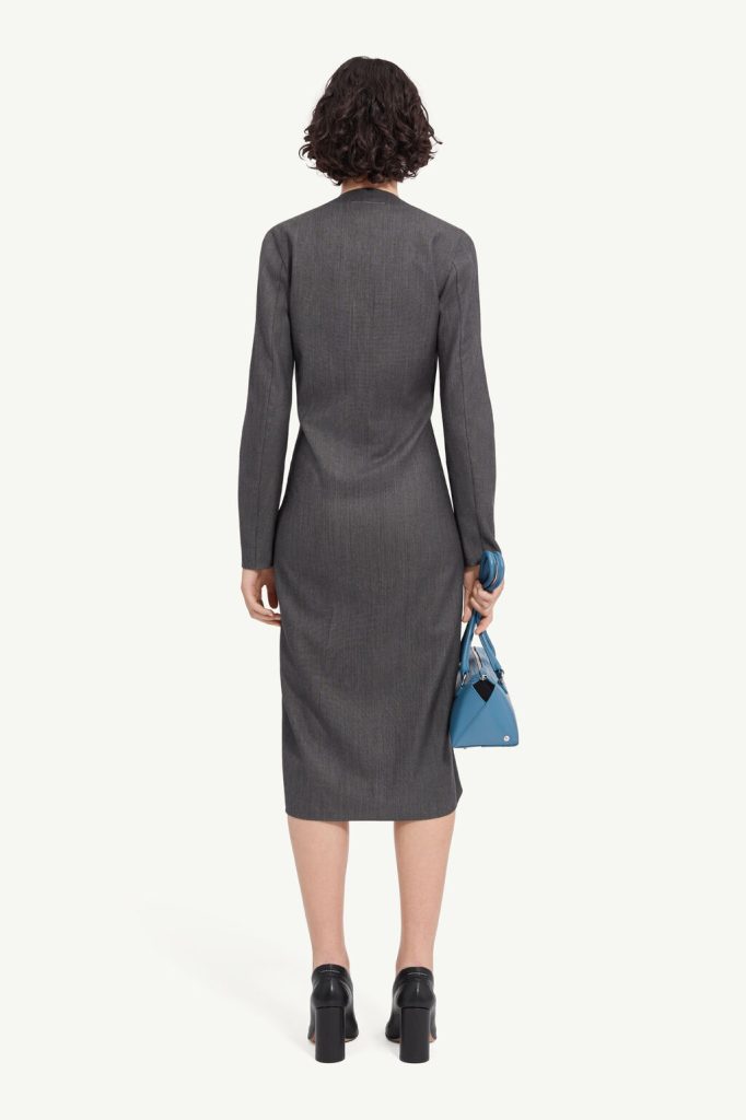 Back view of a woman in a gray knee-length dress with long sleeves, holding a blue handbag and wearing black heeled shoes.
