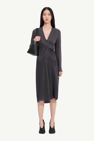 Full-body shot of a woman wearing a dark gray textured midi dress with a front ruching detail, paired with a black handbag and black ankle boots.