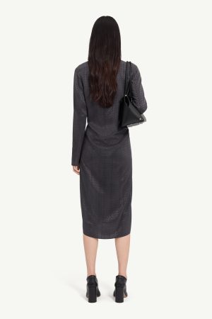 Back view of a woman wearing a dark patterned midi dress with a black shoulder bag and chunky-heeled black shoes.