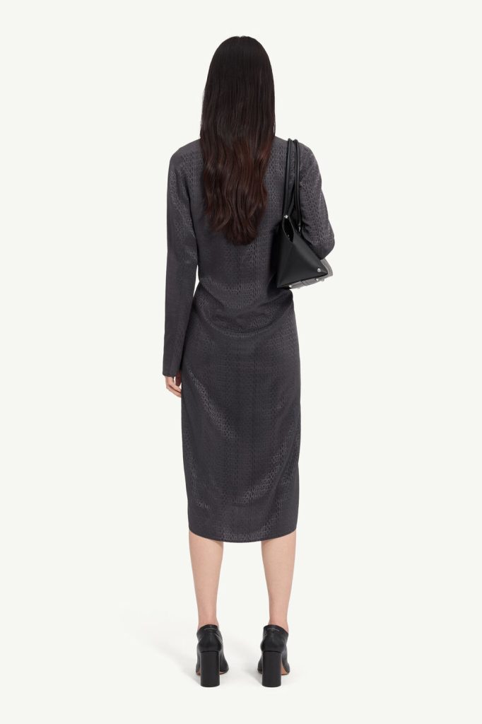 Back view of a woman wearing a dark patterned midi dress with a black shoulder bag and chunky-heeled black shoes.