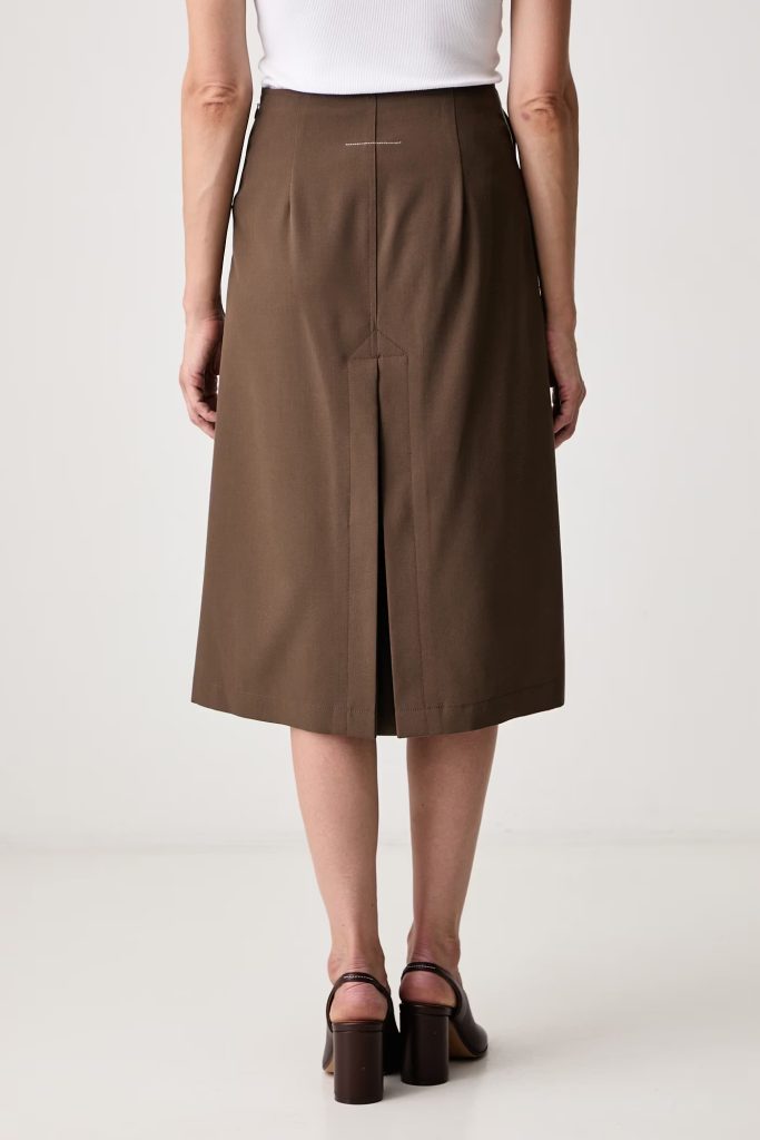 Back view of a person wearing a brown midi skirt with a back vent and stitched detailing, paired with a white top and brown sandals.