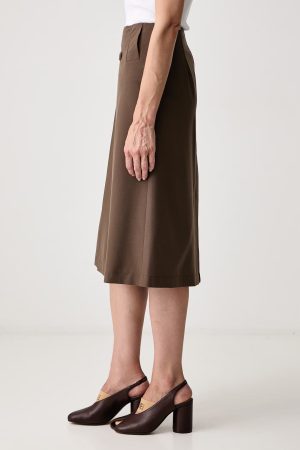 Side view of a person wearing a brown midi skirt with a pleated waist detail, paired with brown block-heeled sandals and a white top.