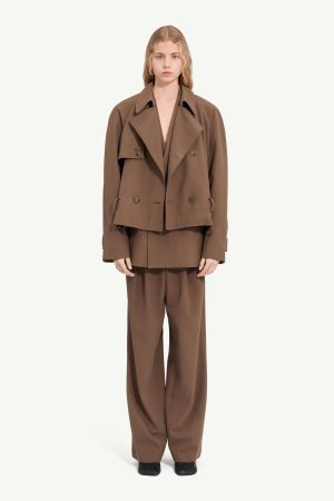 Full-body shot of a model wearing a brown oversized suit: cropped double-breasted jacket with wide lapels and wide-leg trousers against a light neutral background.