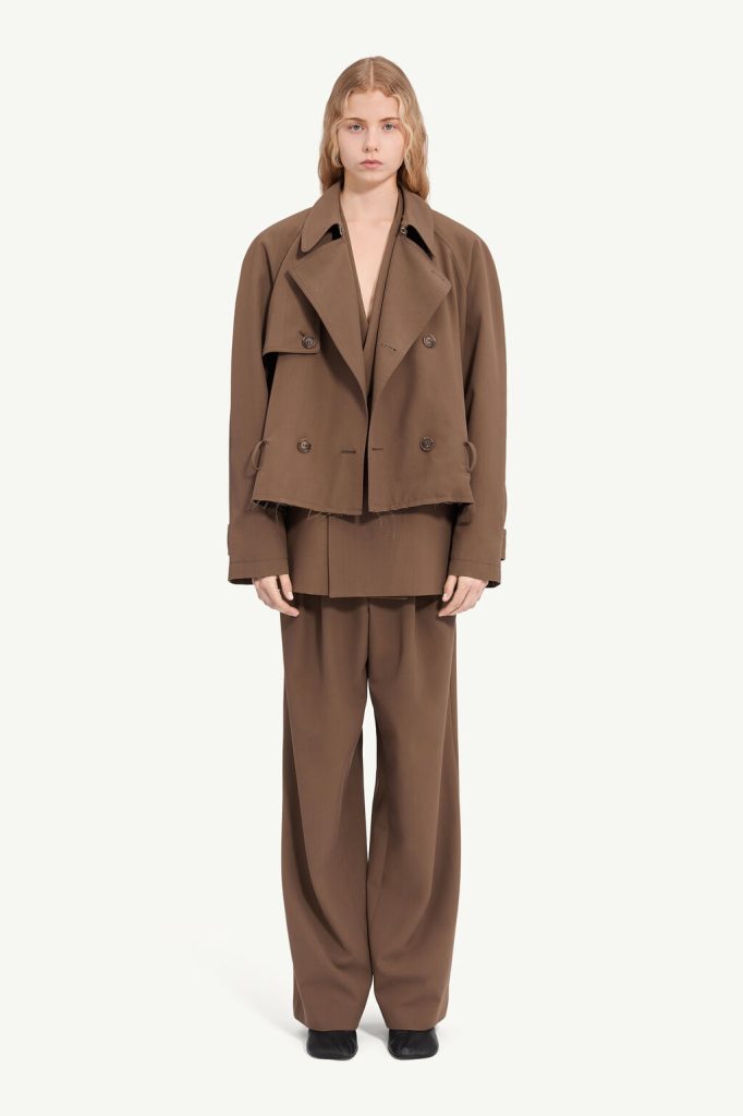 Full-body shot of a model wearing a brown oversized suit: cropped double-breasted jacket with wide lapels and wide-leg trousers against a light neutral background.