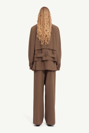 Person with long wavy blond hair, back view, wearing a brown layered trench jacket and matching wide-leg pants.