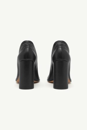 Pair of black leather block-heeled pumps shown from the back, highlighting the chunky heels and stitching detail on the upper.