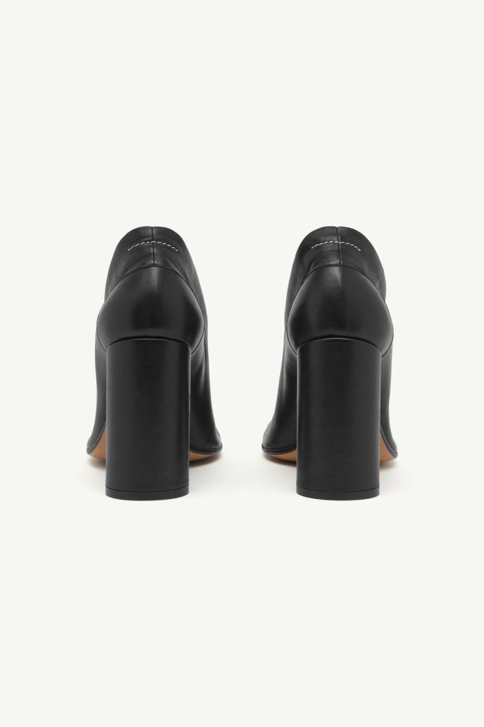Pair of black leather block-heeled pumps shown from the back, highlighting the chunky heels and stitching detail on the upper.