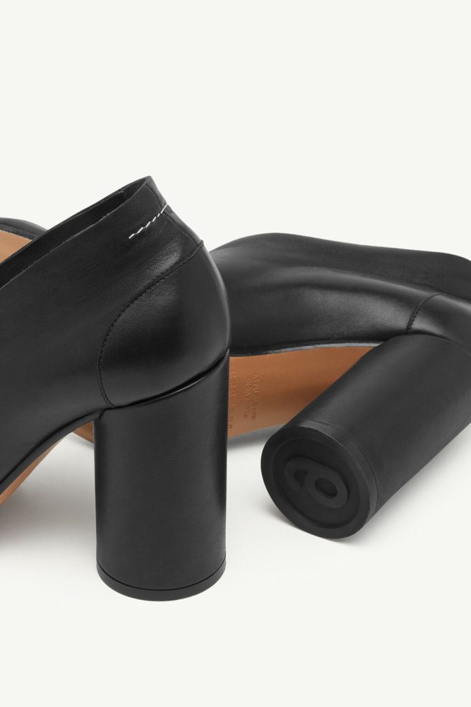 Black leather block-heel mule shown from the back and side, with a tan insole exposed.