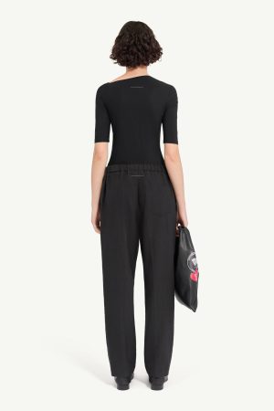 Back view of a person wearing a black short-sleeve top and loose black pants with an elastic waistband, holding a black bag with graphics.