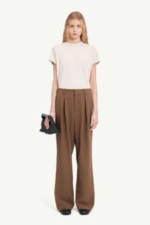 Full-body shot of a woman in a cream T-shirt and brown wide-leg trousers, holding a black clutch.