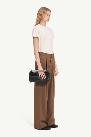 Model in a cream T-shirt and brown high-waisted wide-leg trousers, holding a black handbag with a silver bar handle.