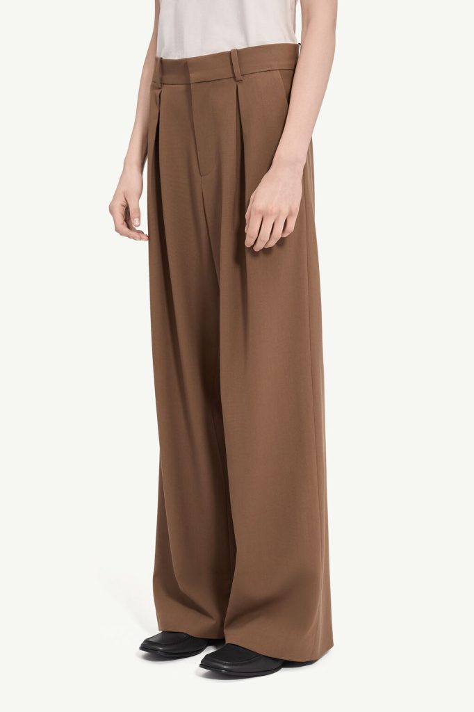 Person wearing high-waisted brown wide-leg trousers with a white top and black loafers, shown from the waist down to feet.