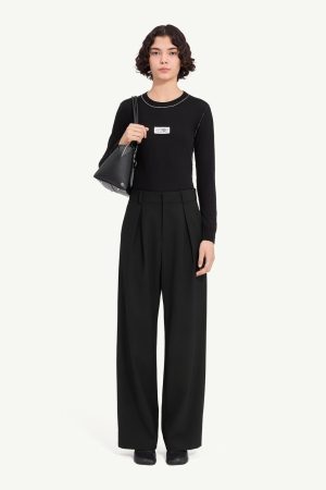 Woman in a black long-sleeve top with white stitching and wide-leg black trousers, carrying a gray shoulder bag.