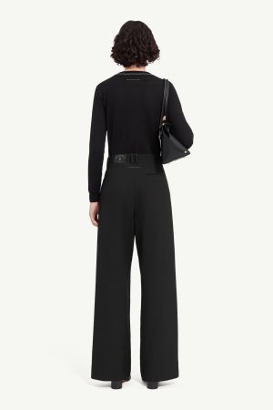 Back view of a person wearing a black long-sleeve top and black wide-leg pants, with a black shoulder bag resting on the left side.
