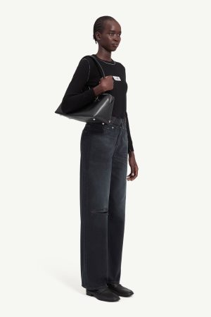 Full-body photo of a Black woman in a black long-sleeved top and dark wide-leg jeans, carrying a black handbag over her shoulder.