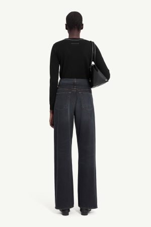Back view of a person wearing a black long-sleeve top and high-waisted wide-leg jeans, carrying a black shoulder bag over the right shoulder.