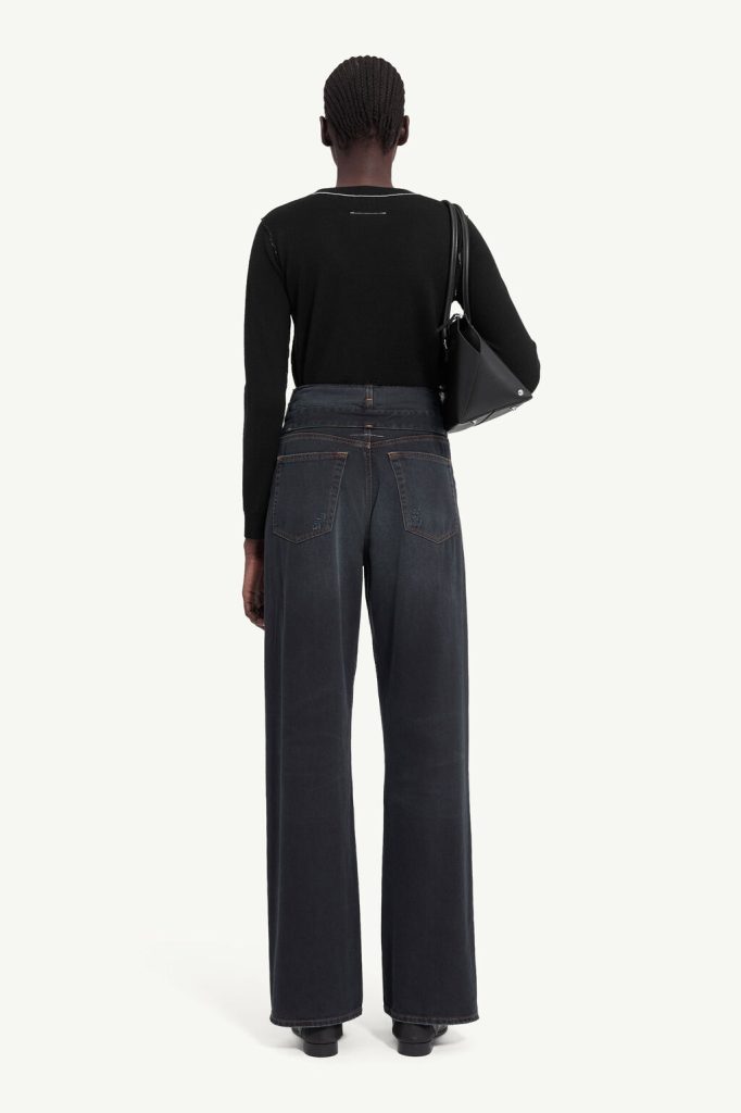 Back view of a person wearing a black long-sleeve top and high-waisted wide-leg jeans, carrying a black shoulder bag over the right shoulder.