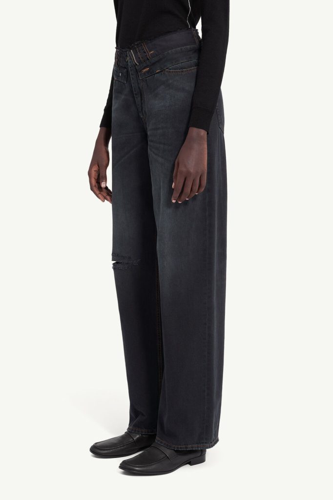 Person wearing dark wash wide-leg jeans with a small knee rip, black top, and black loafers (side view)