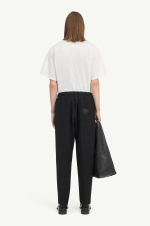 Back view of person in a white T-shirt, black elastic-waist pants, black shoes, carrying a large black tote.
