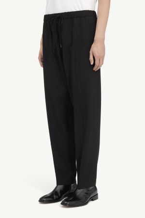 Black wide-leg pants with an elastic drawstring waist, paired with a white top and black leather shoes.