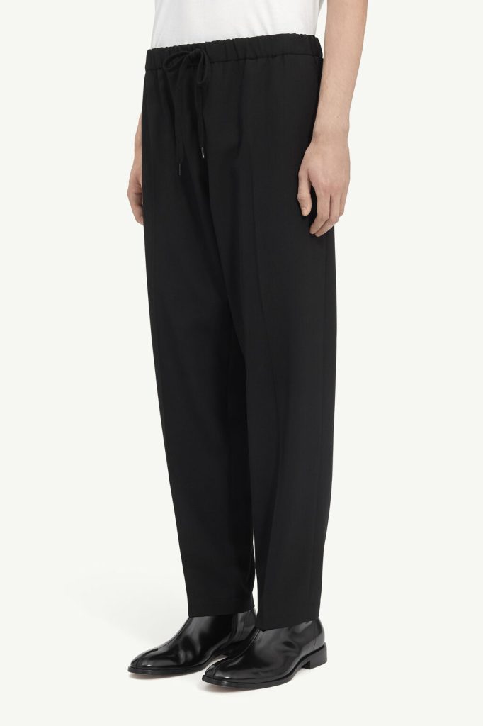 Black wide-leg pants with an elastic drawstring waist, paired with a white top and black leather shoes.