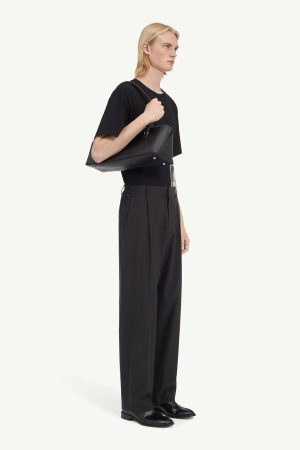 Person in a black t-shirt and wide-leg black pants, carrying a black shoulder bag in a side profile view.