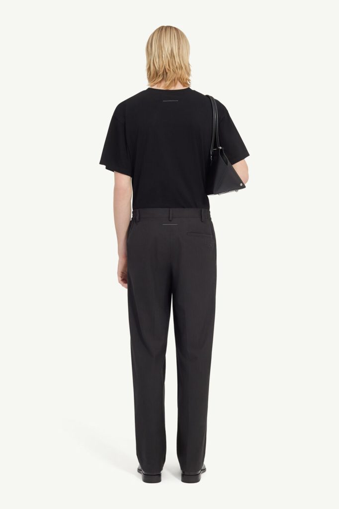 Person viewed from the back wearing a black T-shirt, dark trousers, and a black shoulder bag.