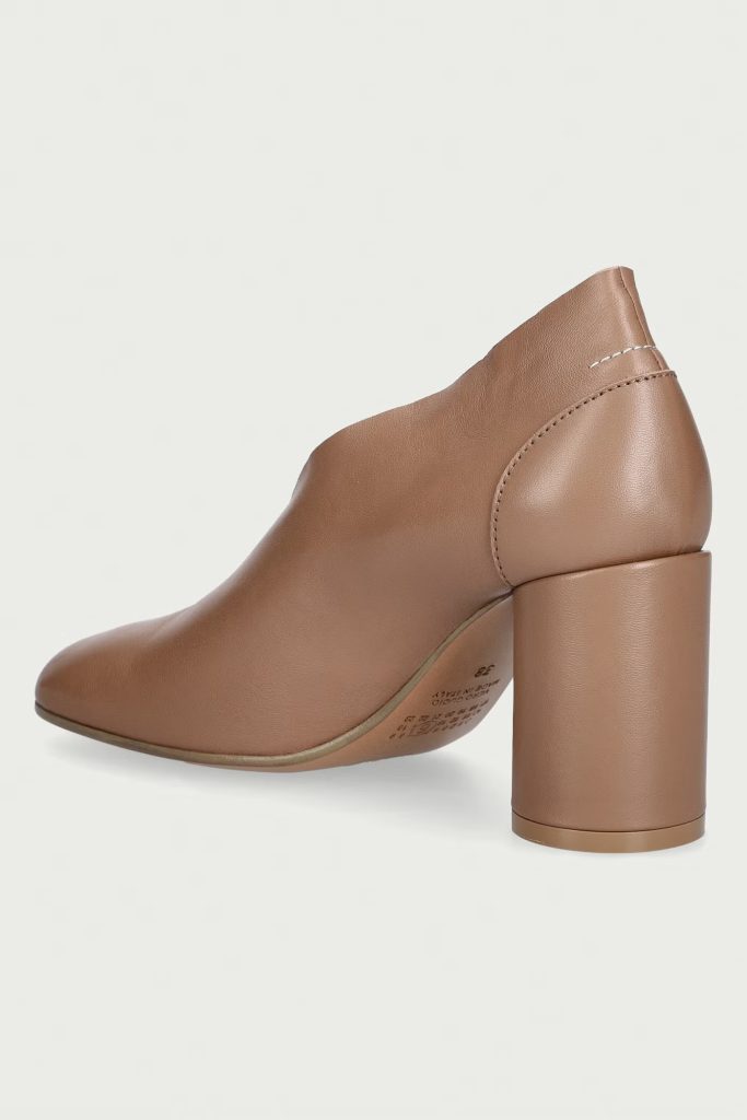 Brown leather pump with a chunky block heel and visible top-stitch seam at the back, shown from a side angle.