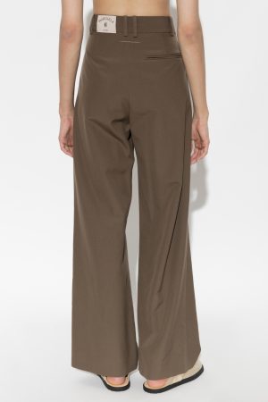 Back view of brown wide-leg tailored pants with belt loops and a small left-rear welt pocket; tag attached at the waistband reads Margiela 6; model wearing beige sandals.