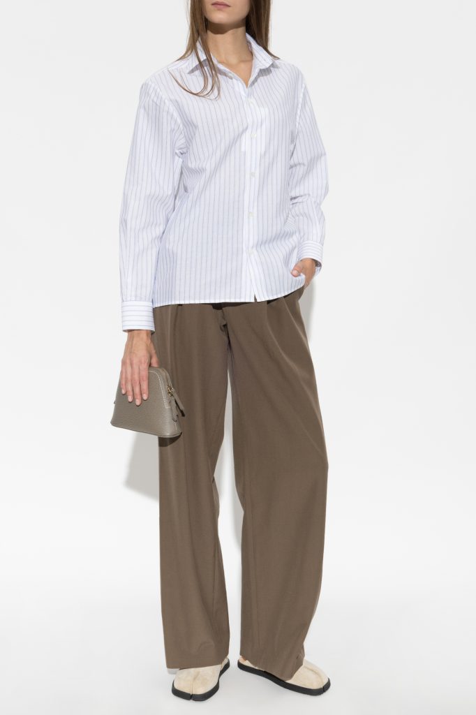 Person wearing a white striped button-up shirt with brown wide-leg pants, holding a small beige handbag.