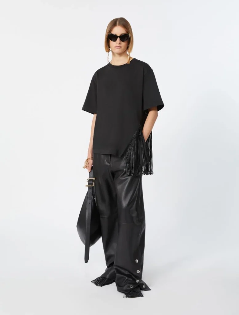 Model in an all-black outfit: oversized T-shirt, wide-leg leather pants, fringed bag, and dark sunglasses.