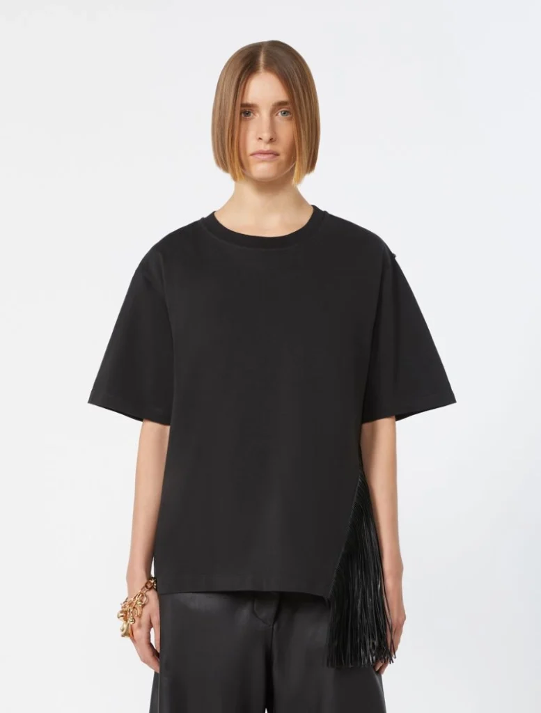 Woman standing in an oversized black T-shirt with a fringe handbag draped at her side, neutral studio background.