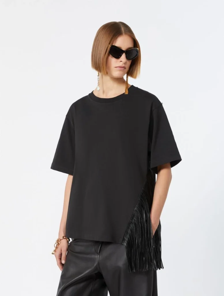 Model wearing an oversized black T-shirt with black leather pants and a long fringe bag on the side, plus cat-eye sunglasses.