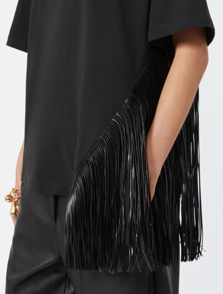 Black fringe handbag slung under the arm with long leather fringe detailing visible beside a black outfit.