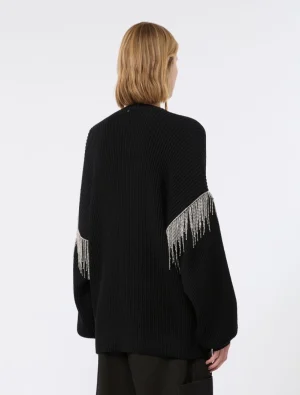 Back view of a person wearing an oversized black knit sweater with beaded fringe along the sleeves, blonde hair visible from behind.