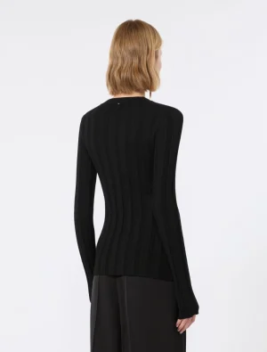 Back view of a person in a black ribbed knit sweater and black pants, blonde hair in a bob, facing away.
