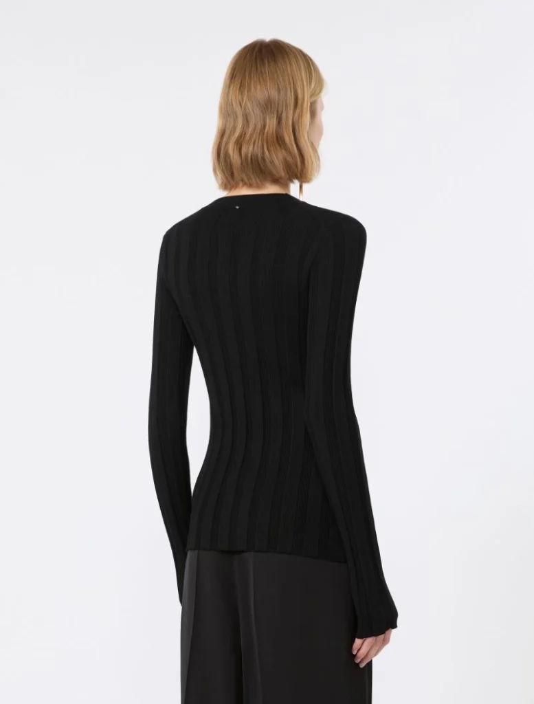 Back view of a person in a black ribbed knit sweater and black pants, blonde hair in a bob, facing away.