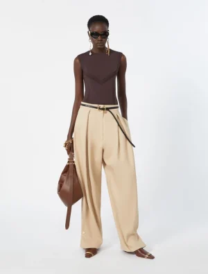 Model wearing a dark brown sleeveless top with cream wide-leg pants, a thin belt, and brown handbag, plus sunglasses.
