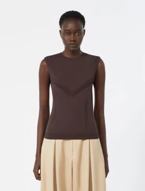 Female model wearing a sleeveless dark brown knit top with chevron V-stitch details, paired with a beige skirt, standing against a light background.
