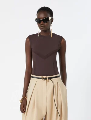Model wearing a sleeveless brown top with chevron stitch details and beige wide-leg trousers, with black sunglasses and gold jewelry.