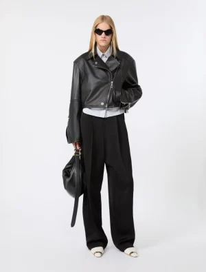 Model in a cropped black leather jacket, white shirt, and wide-leg black trousers with dark sunglasses and a black handbag.